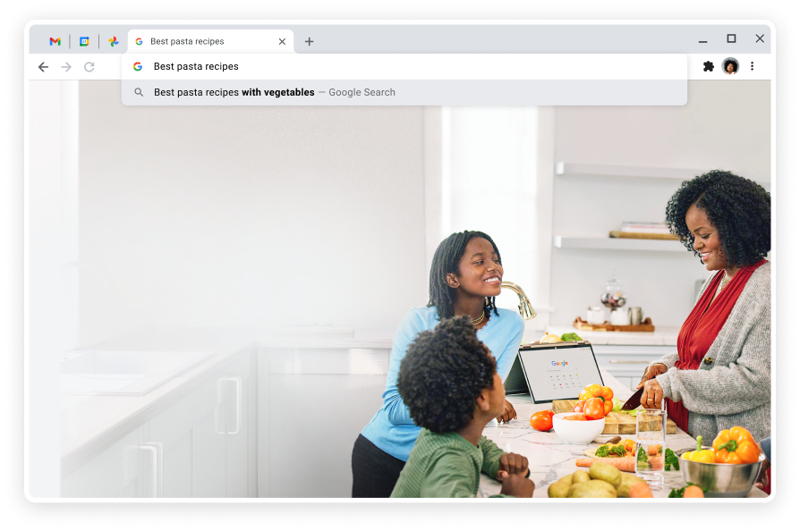 Two children watch an adult cutting vegetables in a white kitchen. A laptop sits on the table with Google search displayed.